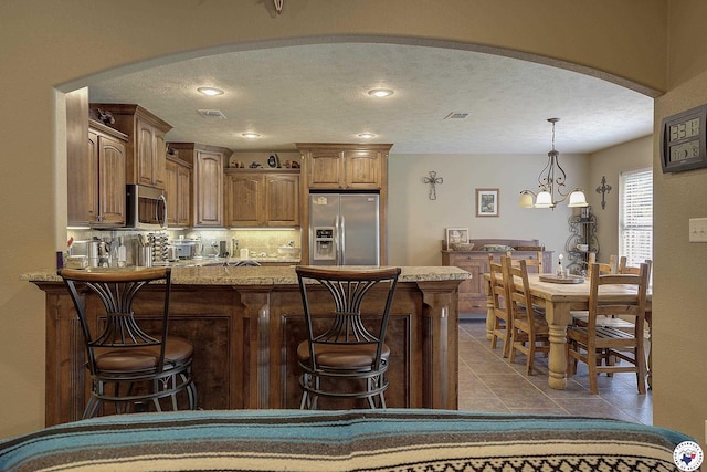 kitchen featuring a breakfast bar area, a textured ceiling, appliances with stainless steel finishes, arched walkways, and a peninsula
