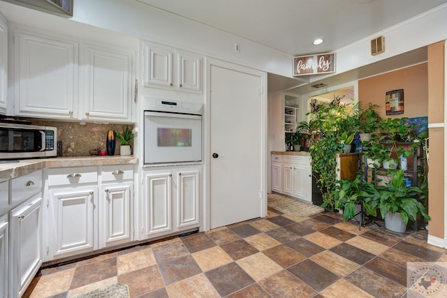 kitchen with backsplash, white cabinets, and oven