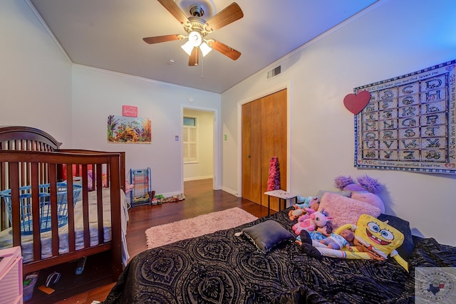 bedroom featuring ornamental molding, a crib, ceiling fan, and dark hardwood / wood-style flooring