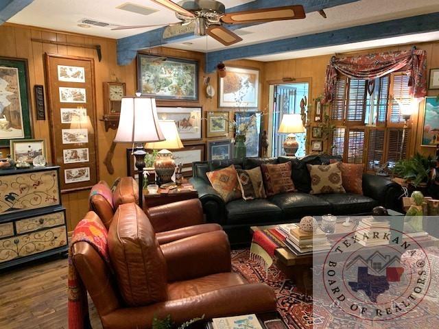 living room with ceiling fan, wooden walls, and wood-type flooring