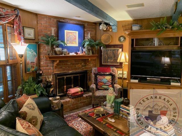 living room with wood walls, beam ceiling, and a brick fireplace