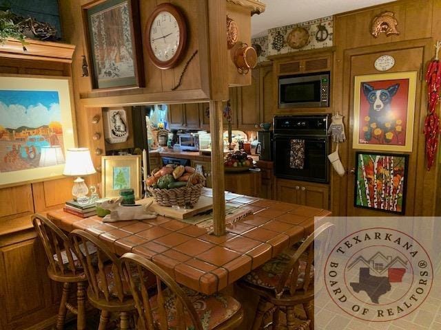 interior space with black oven, tile counters, and wooden walls