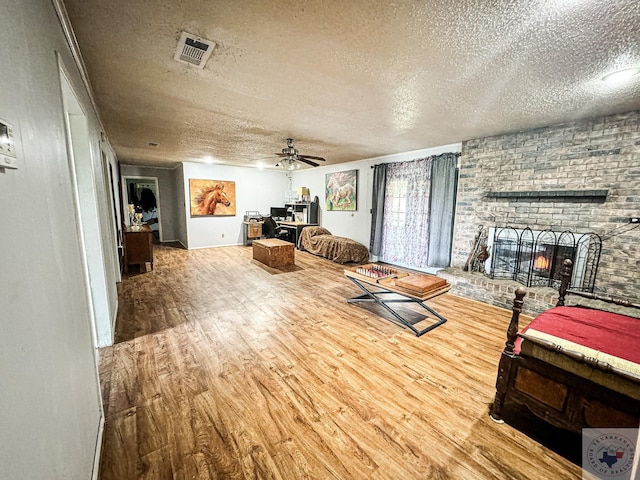 living room featuring ceiling fan, hardwood / wood-style flooring, a brick fireplace, and a textured ceiling