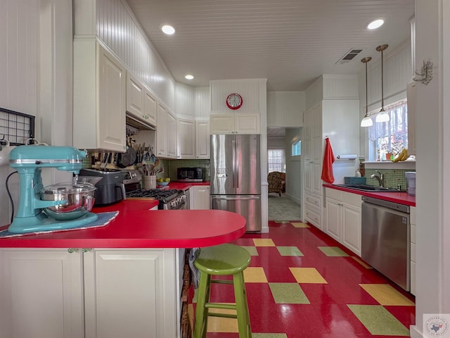 kitchen featuring tile patterned floors, visible vents, a sink, stainless steel appliances, and a peninsula