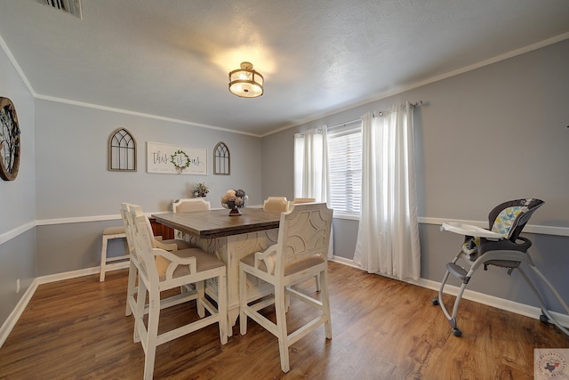 dining space featuring visible vents, baseboards, wood finished floors, and crown molding