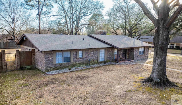 ranch-style house featuring a shingled roof, fence, and brick siding