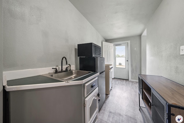 kitchen with black microwave, a textured wall, a sink, and light wood-style flooring