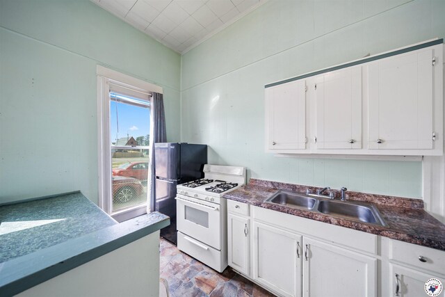 kitchen featuring white cabinets, dark countertops, white gas range oven, and a sink
