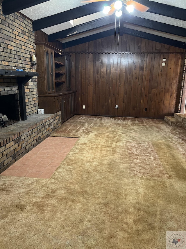 unfurnished living room featuring light carpet, ceiling fan, beam ceiling, a fireplace, and wood walls