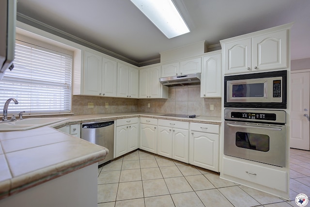 kitchen with under cabinet range hood, light tile patterned floors, a sink, white cabinets, and appliances with stainless steel finishes
