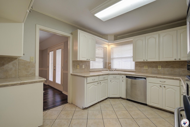 kitchen with dishwasher, light tile patterned floors, a sink, crown molding, and white cabinets