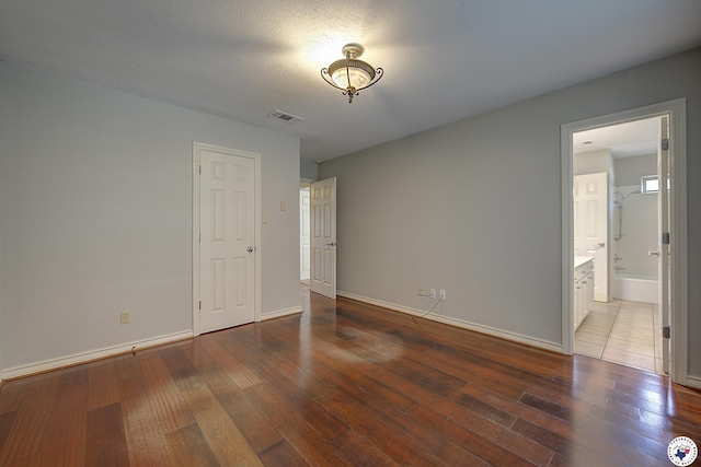 unfurnished bedroom featuring ensuite bath, hardwood / wood-style flooring, baseboards, and visible vents