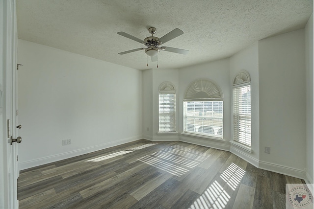 empty room with ceiling fan, a wealth of natural light, dark wood-type flooring, and a textured ceiling