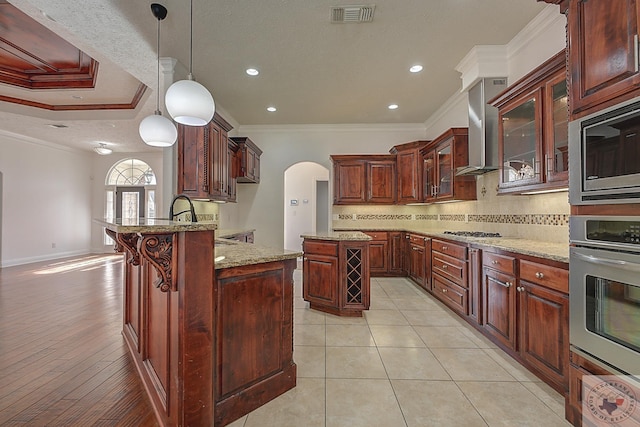 kitchen featuring appliances with stainless steel finishes, decorative light fixtures, ornamental molding, light stone counters, and wall chimney exhaust hood