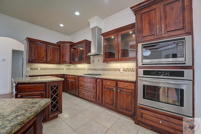 kitchen featuring light stone countertops, appliances with stainless steel finishes, wall chimney exhaust hood, light tile patterned floors, and crown molding