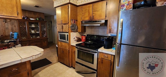 kitchen with decorative backsplash, tile counters, stainless steel appliances, and wood walls