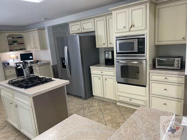 kitchen featuring cream cabinetry, ornamental molding, appliances with stainless steel finishes, and light tile patterned flooring