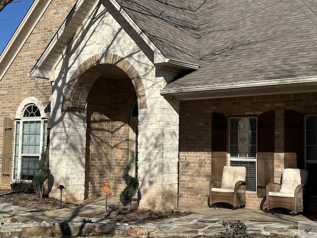 entrance to property featuring a shingled roof, a patio area, and brick siding