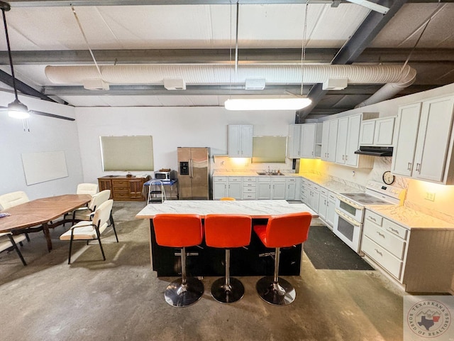 kitchen featuring a kitchen bar, hanging light fixtures, a kitchen island, range with two ovens, and stainless steel fridge