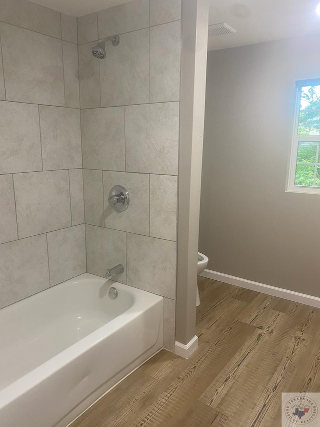 bathroom featuring hardwood / wood-style flooring, tiled shower / bath, and toilet