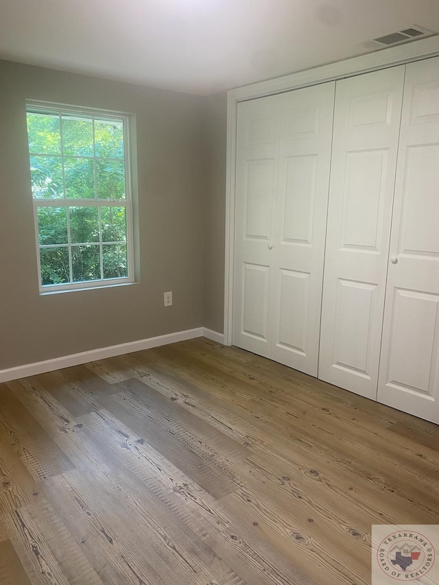 unfurnished bedroom featuring light hardwood / wood-style floors, a closet, and multiple windows