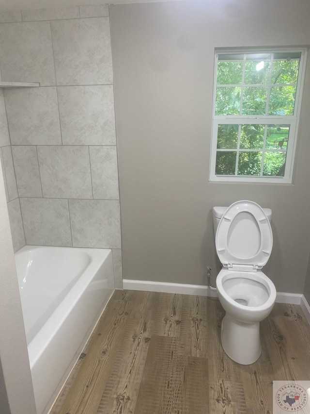 bathroom featuring toilet, hardwood / wood-style floors, and a bath