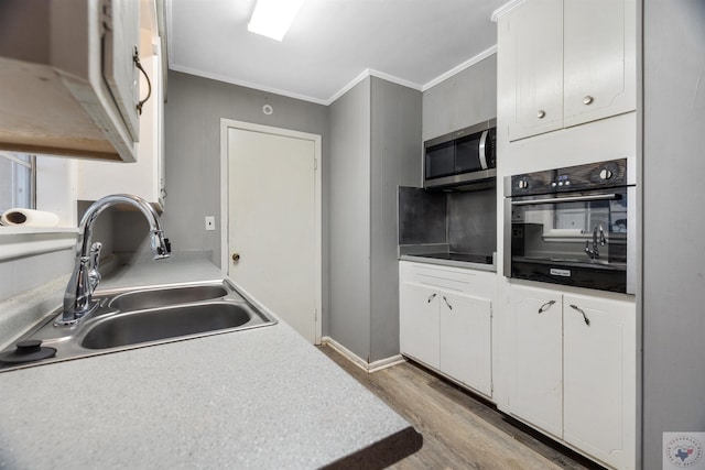 kitchen with crown molding, light hardwood / wood-style flooring, sink, white cabinets, and black appliances