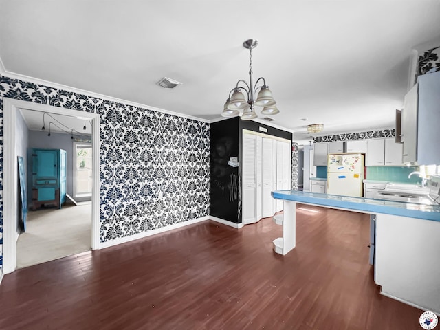 3223 Walnut St, Texarkana, TX 75503 - kitchen with freestanding refrigerator, wallpapered walls, a chandelier, dark wood-type flooring, and white cabinetry