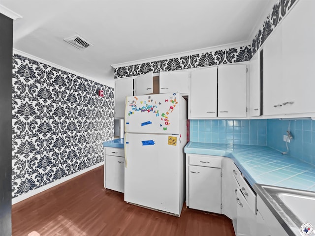 3223 Walnut St, Texarkana, TX 75503 - kitchen featuring freestanding refrigerator, tile countertops, dark wood-type flooring, white cabinets, and ornamental molding