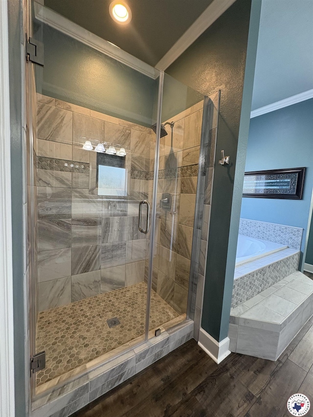 bathroom featuring crown molding, baseboards, wood finished floors, a bath, and a stall shower