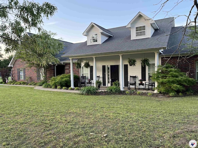 view of front of home featuring roof with shingles, a porch, brick siding, and a front yard