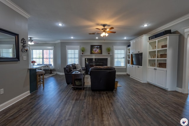 living room featuring a ceiling fan, crown molding, a fireplace, baseboards, and dark wood-type flooring