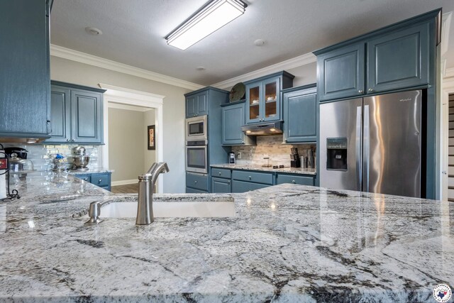 kitchen featuring light stone countertops, a sink, stainless steel appliances, backsplash, and ornamental molding