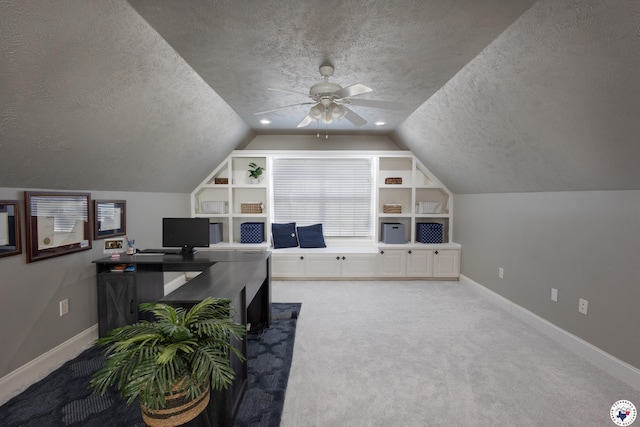 carpeted office with ceiling fan, a textured ceiling, vaulted ceiling, and baseboards