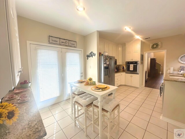 kitchen with white cabinets, appliances with stainless steel finishes, dark stone counters, sink, and light tile patterned floors