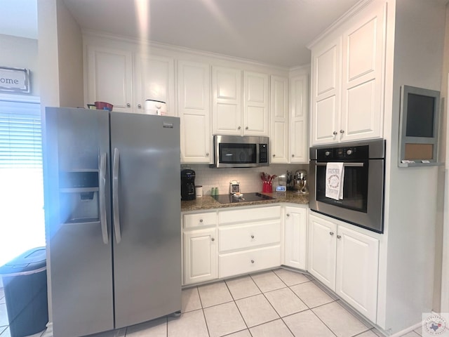 kitchen featuring white cabinetry, stainless steel appliances, dark stone countertops, backsplash, and light tile patterned floors