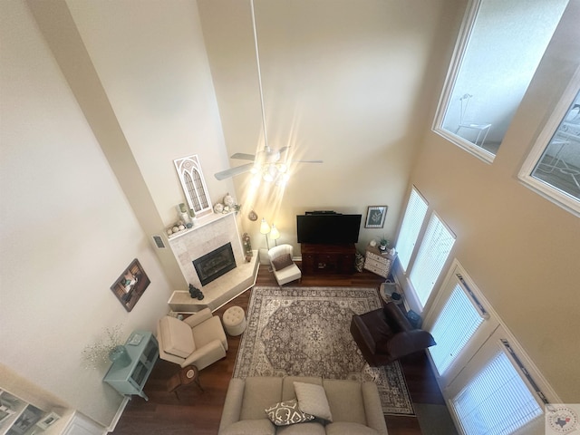 living room with a towering ceiling, ceiling fan, hardwood / wood-style floors, and a fireplace