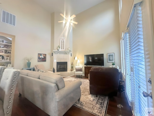 living room featuring built in shelves, a high ceiling, a tile fireplace, and dark hardwood / wood-style flooring