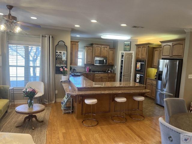 kitchen with black appliances, tasteful backsplash, brown cabinetry, a kitchen bar, and crown molding