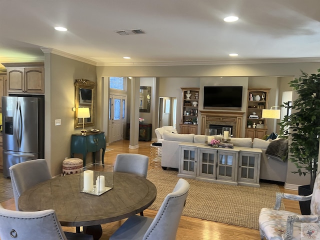 dining space featuring light wood finished floors, visible vents, a glass covered fireplace, ornamental molding, and recessed lighting