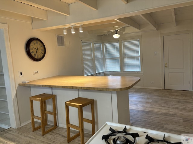 kitchen featuring light hardwood / wood-style flooring, beamed ceiling, kitchen peninsula, and a kitchen bar