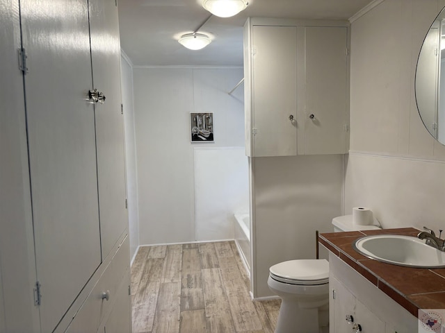 bathroom with wood-type flooring, crown molding, toilet, and vanity