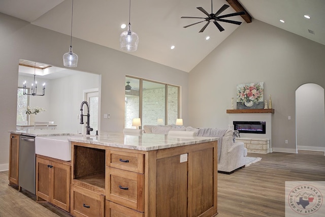 kitchen featuring sink, light stone counters, decorative light fixtures, stainless steel dishwasher, and a kitchen island with sink