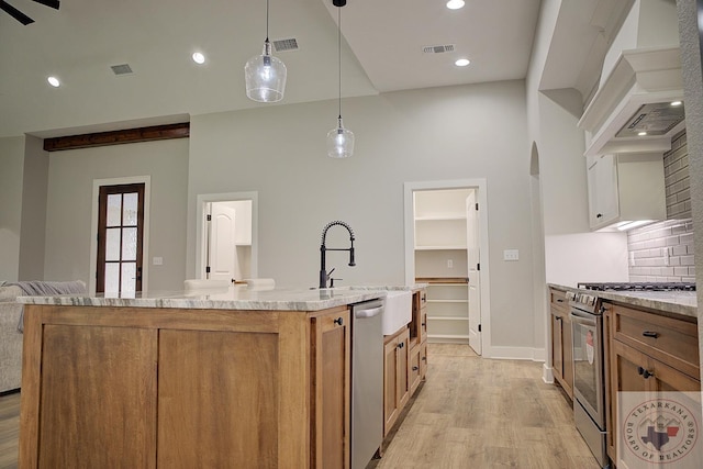 kitchen featuring pendant lighting, sink, a kitchen island with sink, stainless steel appliances, and custom range hood