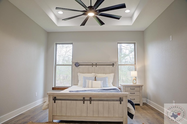 bedroom with ceiling fan, a tray ceiling, and light hardwood / wood-style flooring