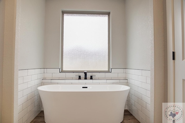 bathroom featuring a healthy amount of sunlight, a tub to relax in, and tile walls