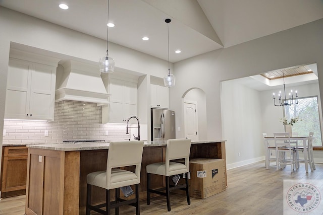 kitchen featuring custom exhaust hood, white cabinetry, and a center island with sink