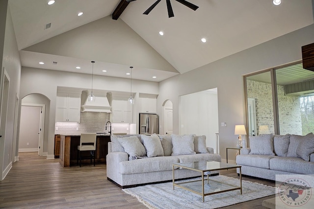 living room with sink, ceiling fan, hardwood / wood-style floors, high vaulted ceiling, and beamed ceiling