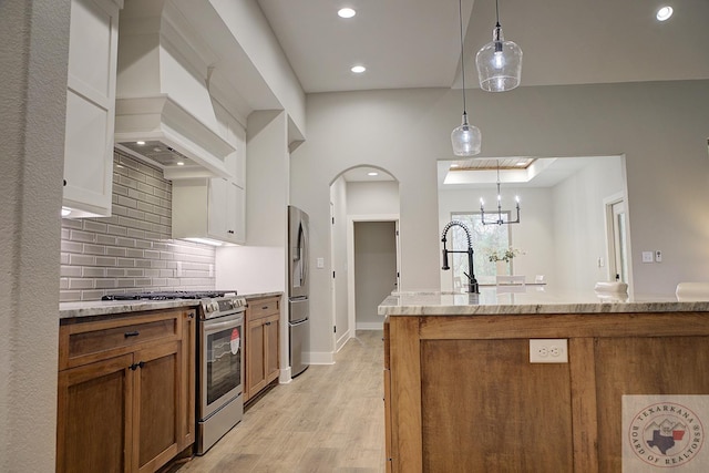 kitchen featuring tasteful backsplash, light stone counters, decorative light fixtures, appliances with stainless steel finishes, and white cabinets