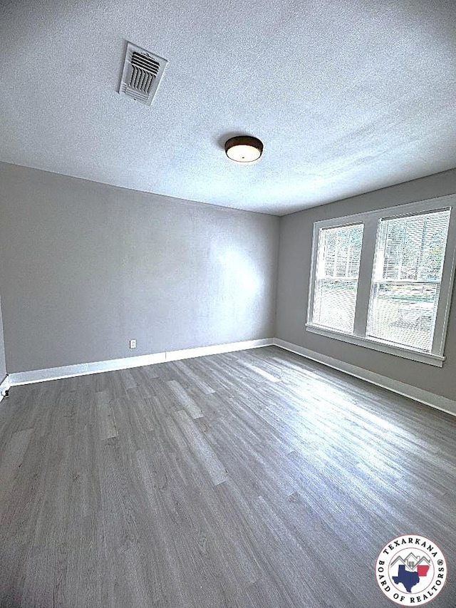spare room with a textured ceiling, baseboards, visible vents, and dark wood-style floors